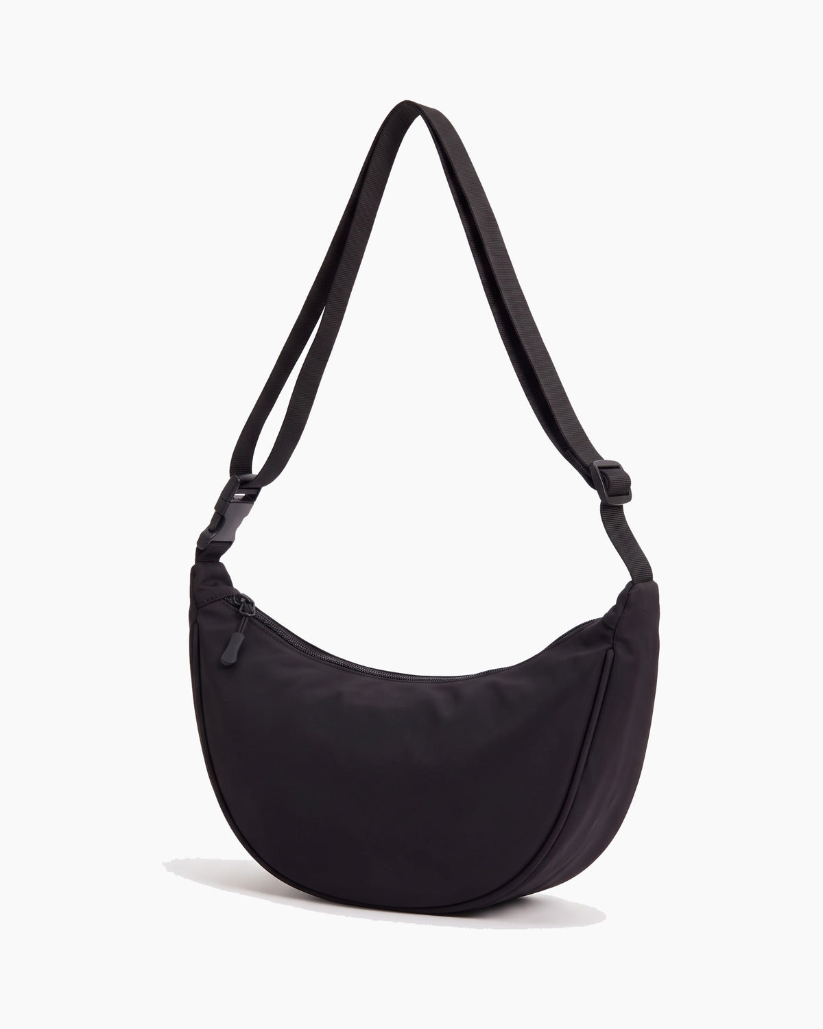 Black sling bag turned to show its depth and side, on a plain background