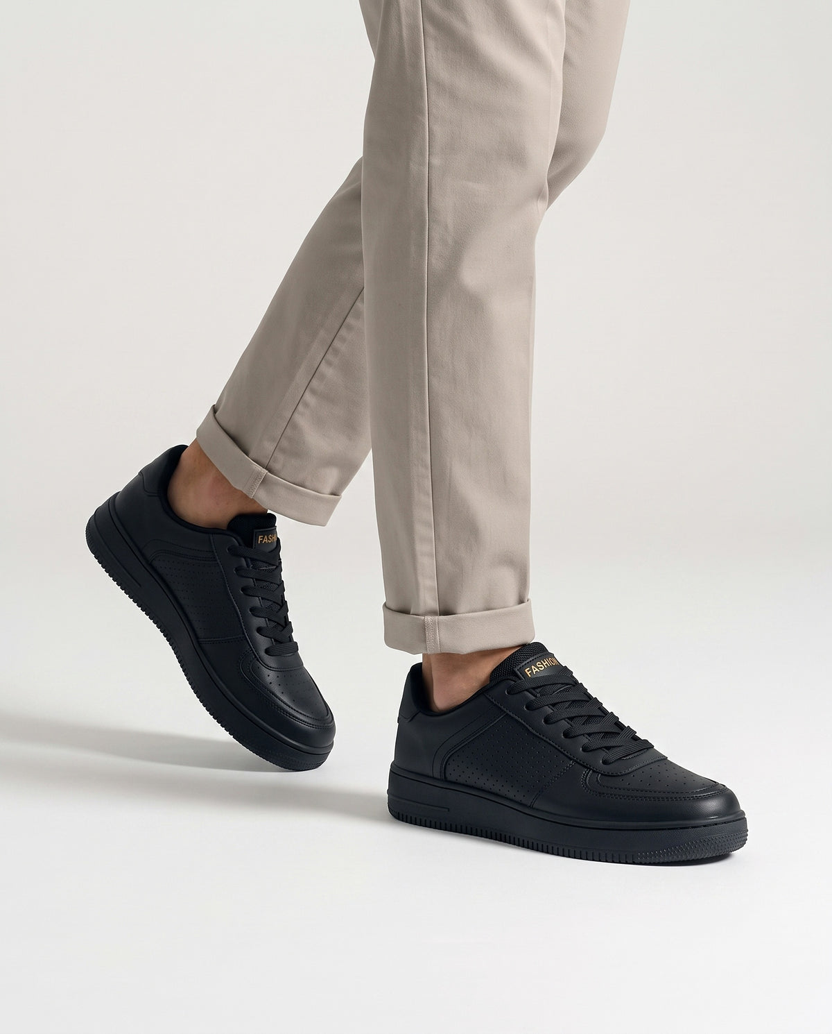 Model mid-stride wearing black low top sneakers with neutral stone chinos, studio