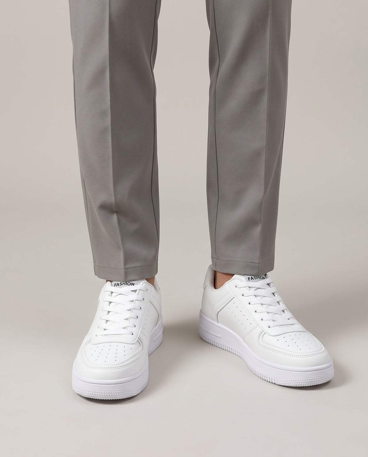 Model wearing white low top sneakers with neutral stone chinos, studio