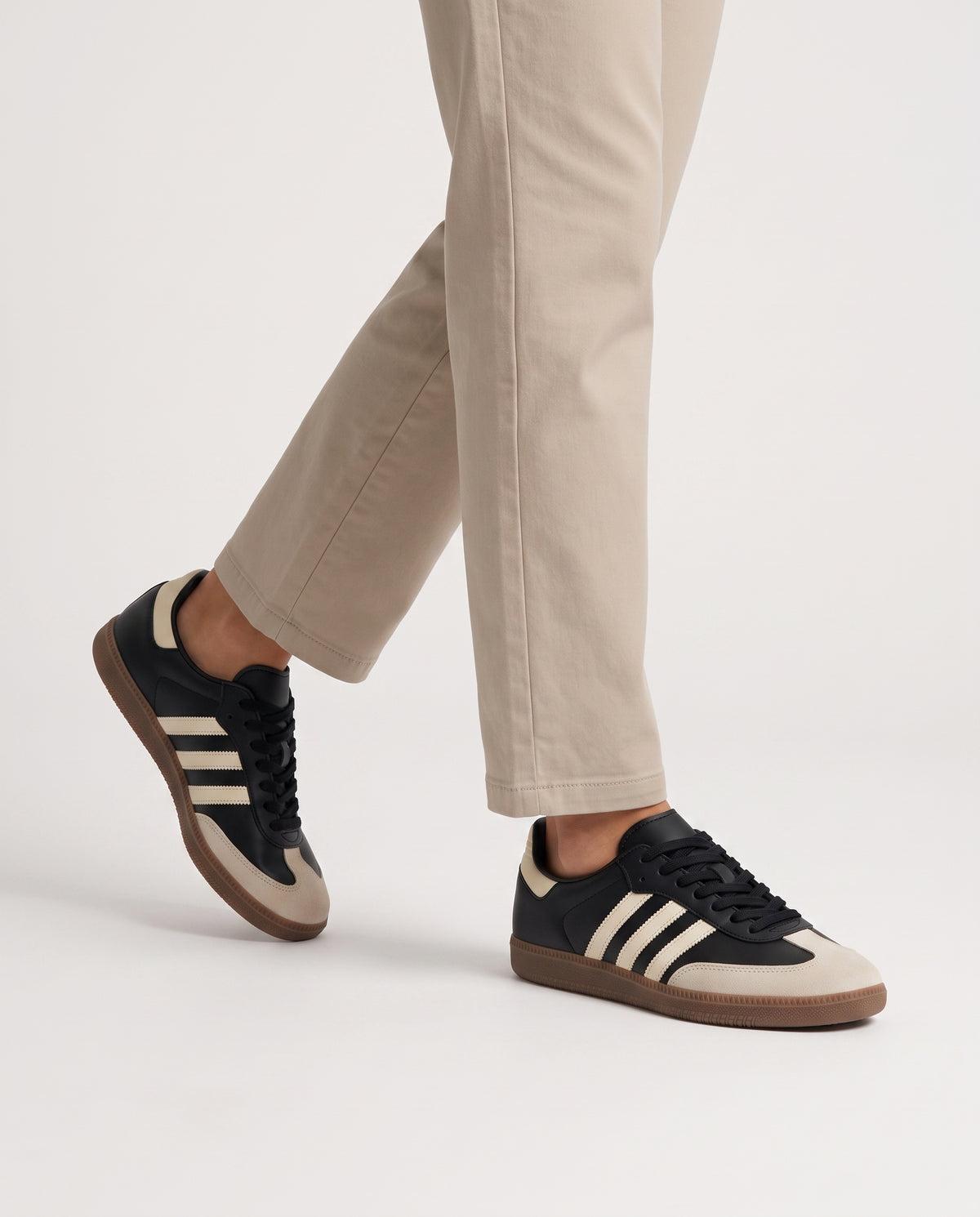 Model mid-stride wearing black retro low top sneakers with neutral stone chinos, studio