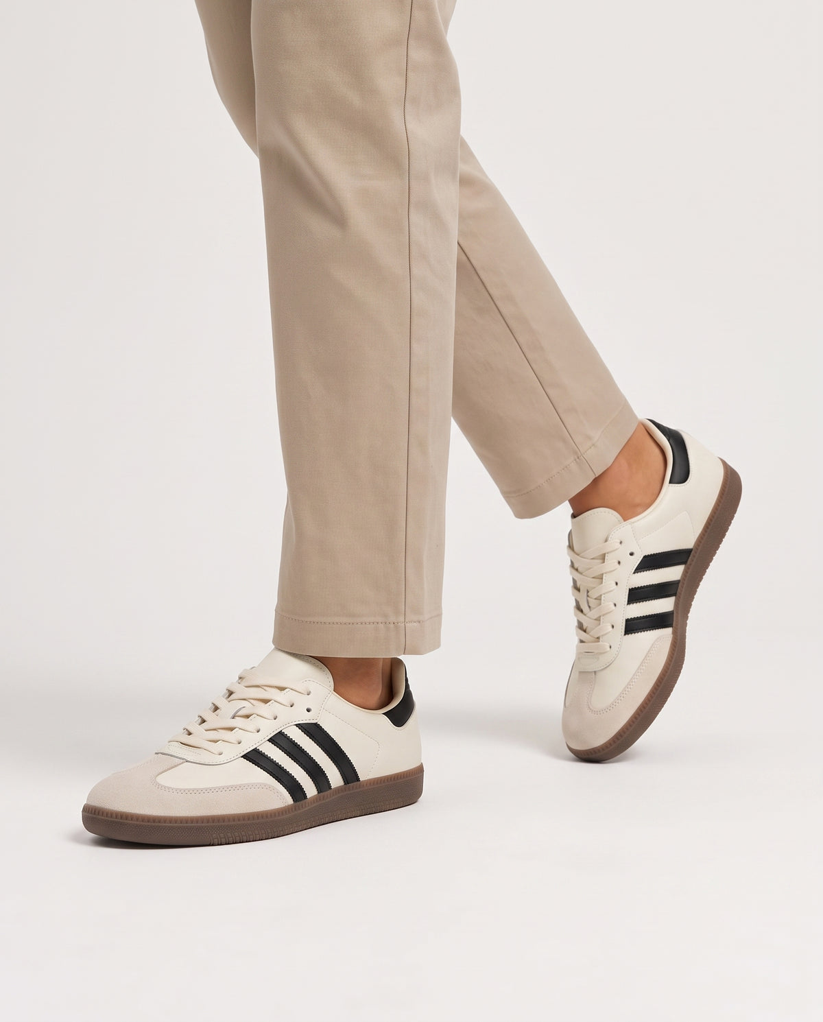 Model mid-stride wearing cream retro low top sneakers with neutral stone chinos, studio