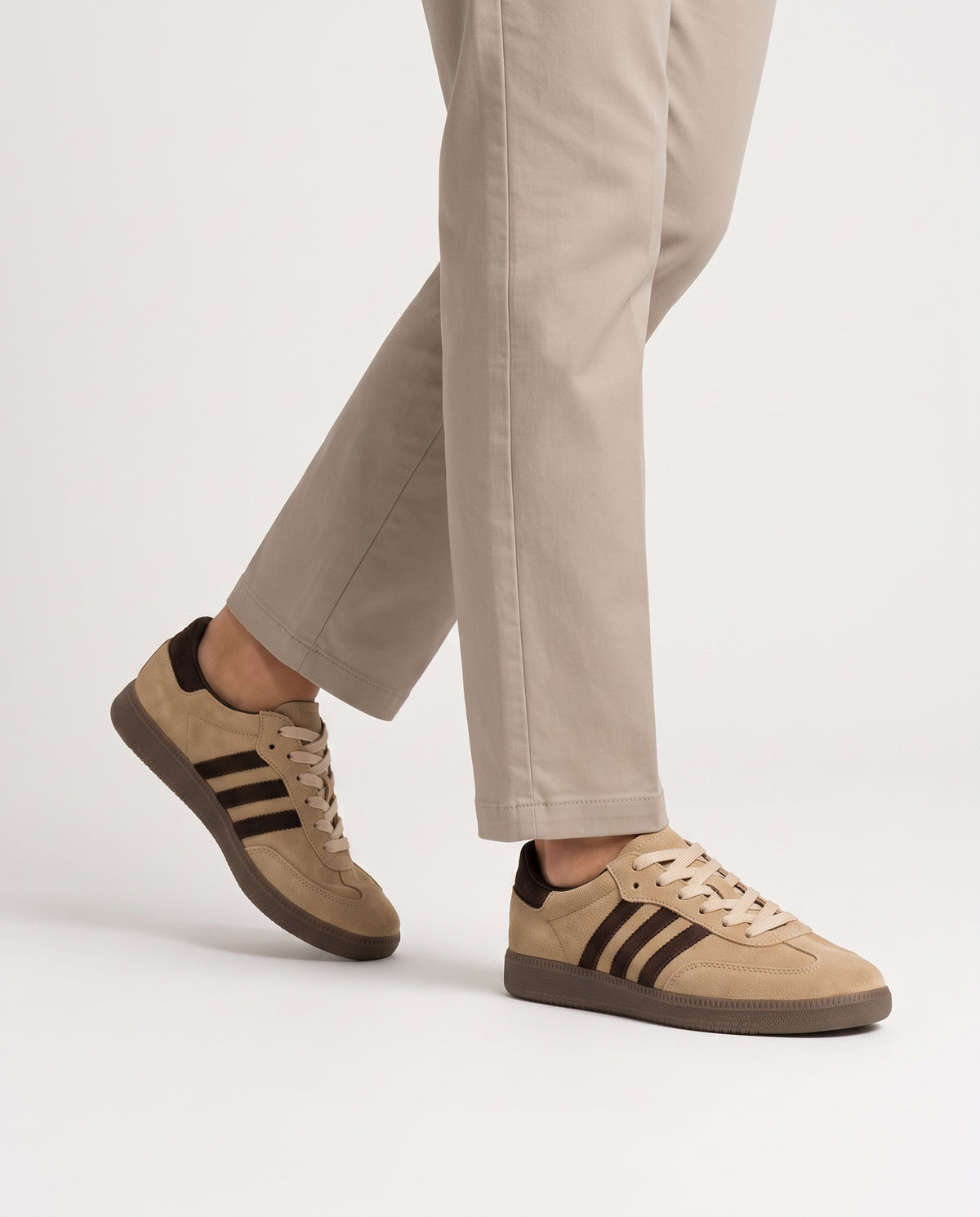 Model mid-stride wearing camel suede retro low top sneakers with neutral stone chinos, studio