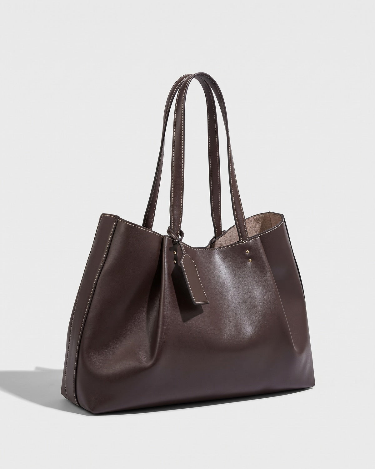 Brown slouchy tote bag with contrast topstitching and twin handles, three-quarter view on a plain background